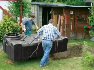 Twee mannen installeren eenvoudig een platte septic tank in een tuin zonder zware machines.