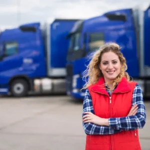 Vrouw in rode bodywarmer met blauwe vrachtwagens op de achtergrond, ideaal voor bedrijven die een AdBlue® tank willen kopen voor efficiënt brandstofbeheer.